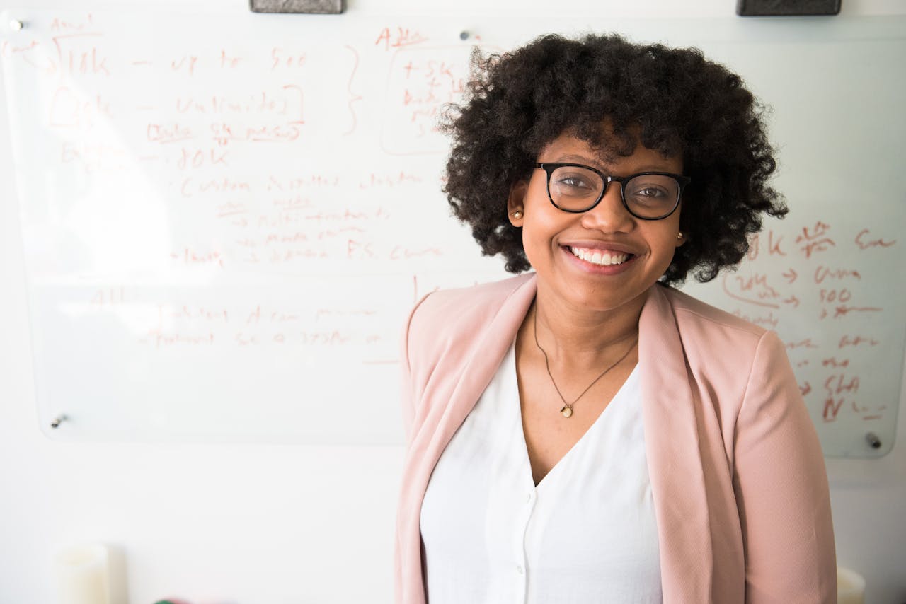 Aidants familiaux : comment ne pas s’épuiser dès les premiers mois ? Smiling businesswoman with glasses and afro hairstyle in an office setting.