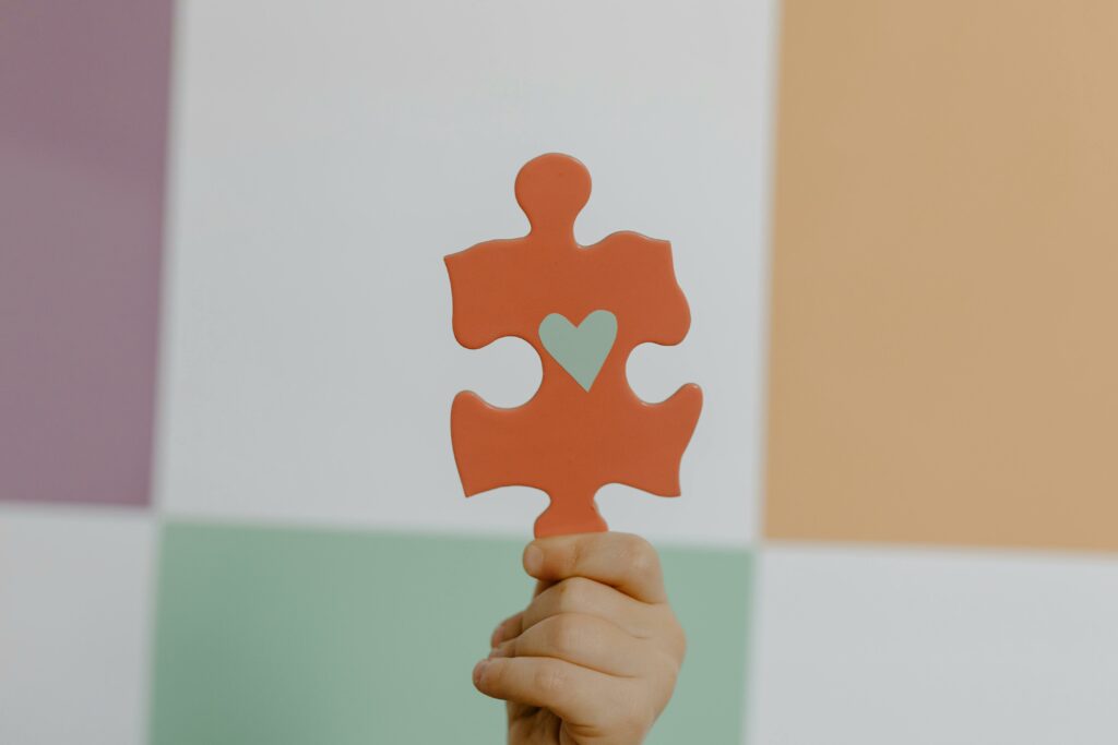 A hand holds a red puzzle piece with a heart, symbolizing connection and awareness.